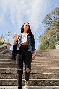 年轻女在户外散步时拿着咖啡喝的肖像城市概念图片