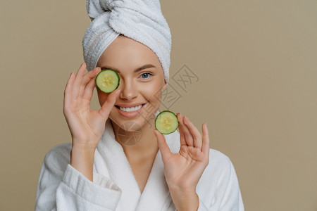 正面的清新美容貌女拿着新鲜黄瓜片面罩部皮肤上装着内衣浴巾头部裹着图片