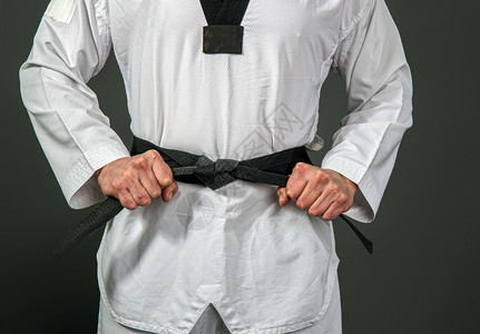 白色台拳道和服的强壮男运动员将黑带系在感知的上图片