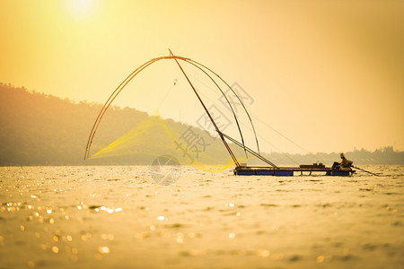 亚洲渔网利用木船在河上投下净日落或的木船侧影鱼网海上有山地岛屿背景的侧影鱼网图片
