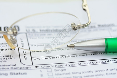 一对眼镜和绿钢笔在所得税申报表上图片