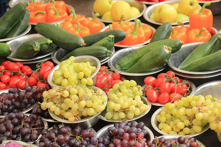 市场摊位上新鲜水果和蔬菜小金属碗中展示的葡萄西红柿椰菜和胡椒图片