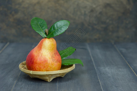 红梨子绿色叶放在木制桌边的篮子上图片