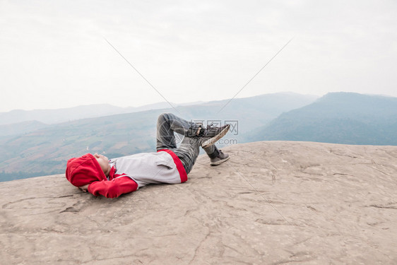 时髦的亚洲男人在岩石中放松时髦的亚洲男人在蓝天映衬下的岩石山顶上放松图片