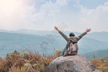 穿着背着包的坐在山顶岩石上与天空的蓝色相对图片