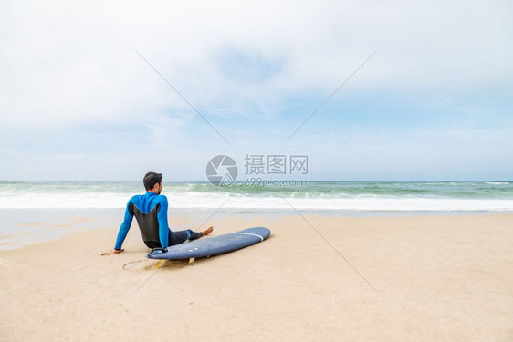 年轻男冲浪者穿着泳衣早上冲浪课后坐在海滩上的冲浪板旁图片