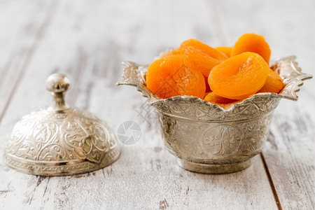在木制白桌上传统银碗里干枯的杏子图片