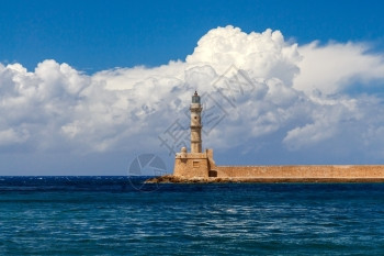 在古老的Chania港的灯塔蓝海和云彩的背景之下图片