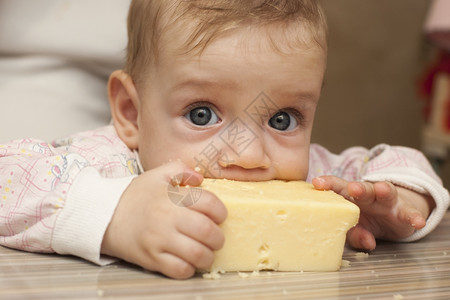 婴儿坐在桌子上吃了一块奶酪图片