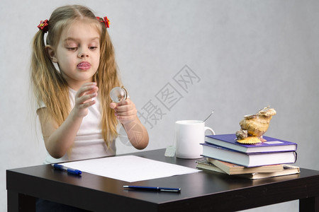 女孩若有所思毫不费力地转动一个小玻璃球坐在桌边墓中有书籍纸张钢笔玻璃球一杯茶贝壳作者的形象图片