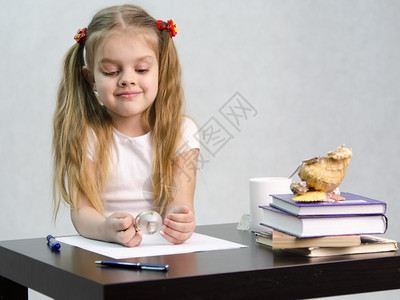 女孩若有所思毫不费力地转动一个小玻璃球坐在桌边墓中有书籍纸张钢笔玻璃球一杯茶贝壳作者的形象图片