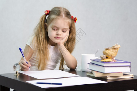 女孩坐在桌子旁在一张纸上写字墓中有书籍纸张钢笔玻璃球一杯茶贝壳作者的形象图片