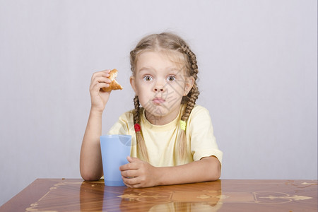 四岁女孩坐在桌子上吃松饼喝塑料杯酒图片