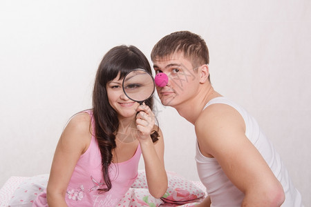 年轻夫妇坐在床上与放大玻璃和小丑鼻子玩得开心图片
