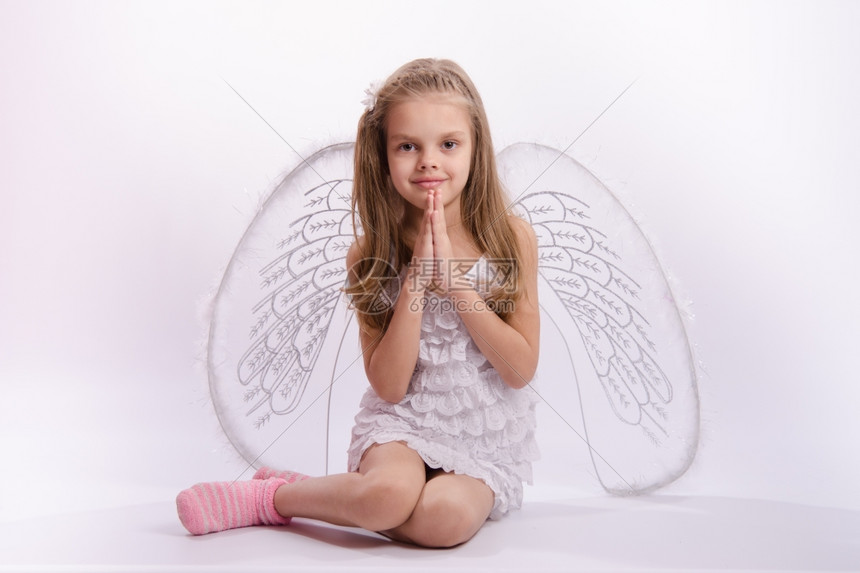 6岁女孩穿着明亮的天使服装白色背景上有翅膀坐着女孩穿手折叠的天使服装图片