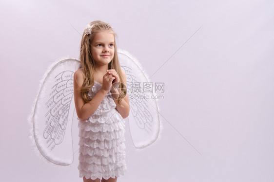 6岁女孩身着一明亮的天使服装白色背景上有翅膀女孩打扮成天使双手折叠着翅膀图片