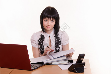 坐在呼叫中心的桌子上可爱小女孩穿着笔记本电脑穿着白衬衫带文件图片
