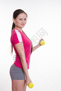 年轻美丽的女孩接受欧洲人的体育锻炼运动员进行两只哑铃的锻炼图片