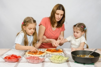 妈和两个女儿在厨房餐桌前准备做比萨饼图片