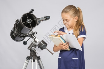 女学生天文家在书本上叶子寻找在望远镜台的正确信息图片