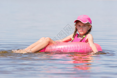 坐在游泳圈上河里漂浮上身着帽子的悲哀女孩图片