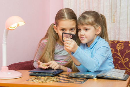 两个孩子透过放大镜观察硬币图片