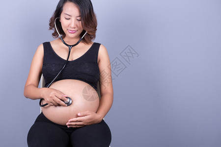 怀有听诊器的怀孕的亚洲妇女倾听肚子婴儿的图片