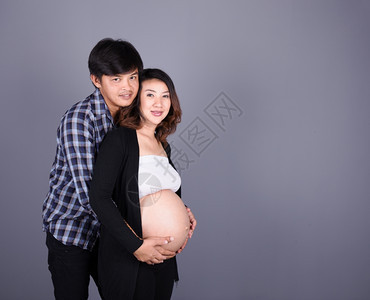 年轻夫妇母亲怀孕父快乐身穿灰墙图片