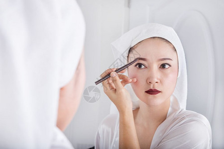 美丽的女人看着镜子用铅笔化妆眉毛图片