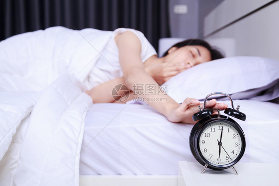 女人靠在床上举起手来关掉卧室的闹钟图片