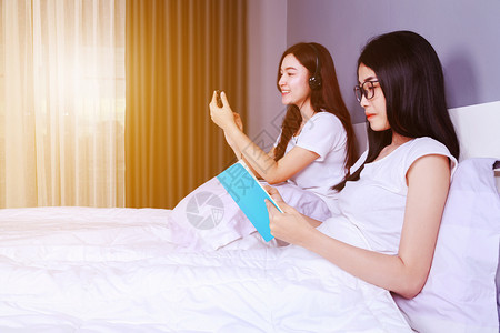 2名妇女在卧室的床上看书和使用智能手机图片