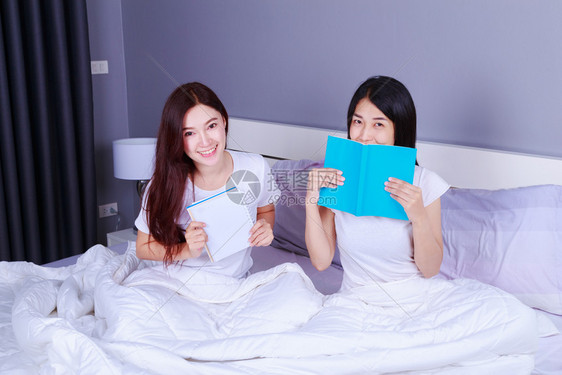 两个女人在卧室的床上写和读一本书图片
