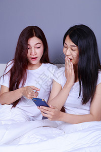 两个惊吓的女人在卧室床上用手机图片