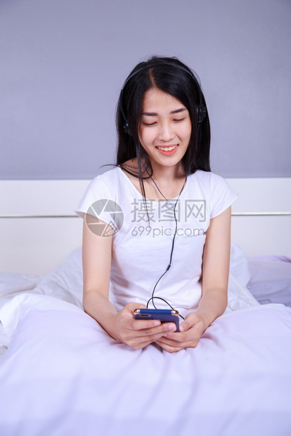女用耳机在卧室的床上监听智能手机的音乐图片
