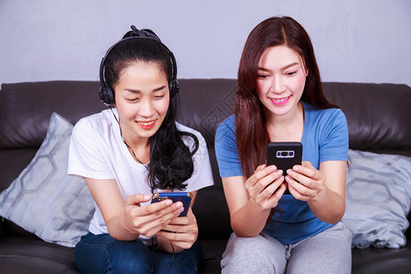 两位年轻女子在家沙发上用耳机和乌鸦在沙发上一起收听音乐图片