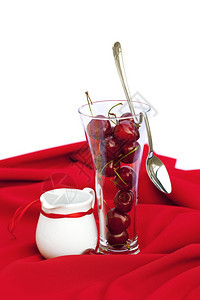 配有樱桃和勺子的牛奶罐红底背景图片