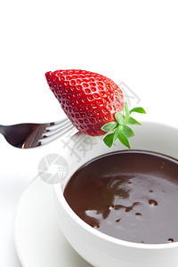 在杯子叉和草莓中融化的巧克力在白色上隔绝图片