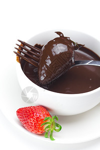 在杯子叉和草莓中融化的巧克力在白色上隔绝图片