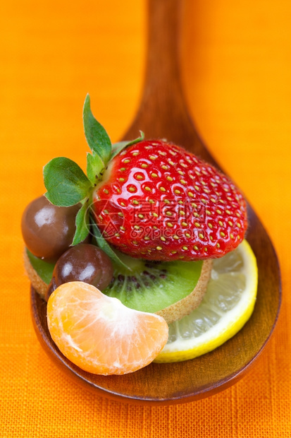 草莓番茄柑橘柠檬和巧克力糖放在橘子织物的木勺中图片