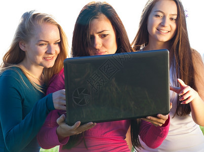 三名美丽的年轻女士手持笔记本电脑在球场上天空背景图片