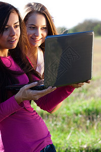 三名美丽的年轻女士手持笔记本电脑在球场上天空背景图片