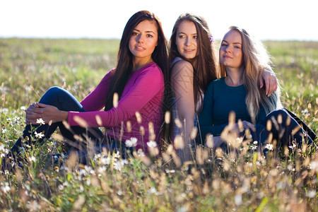 三位美丽的年轻女士坐在天空背景的田地上图片