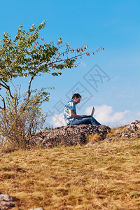 年轻人用笔记本电脑坐在山上面对蓝天图片