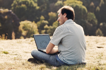 年轻人用笔记本电脑坐在山坡的草地上图片