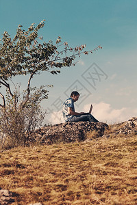 年轻人用笔记本电脑坐在山上面对蓝天图片