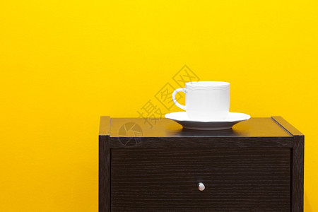 坐在床边的桌子上用杯对着公寓的黄色墙壁图片