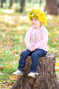 美丽的小女孩戴着枫叶的花环坐在树桩上图片