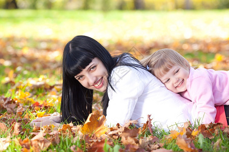 美丽的年轻母亲和女儿躺在秋叶树上图片
