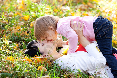 美丽的年轻母亲和女儿躺在秋叶树上图片