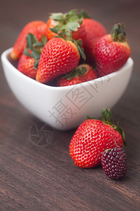 碗里的红色多汁草莓和木头表面的黑莓图片
